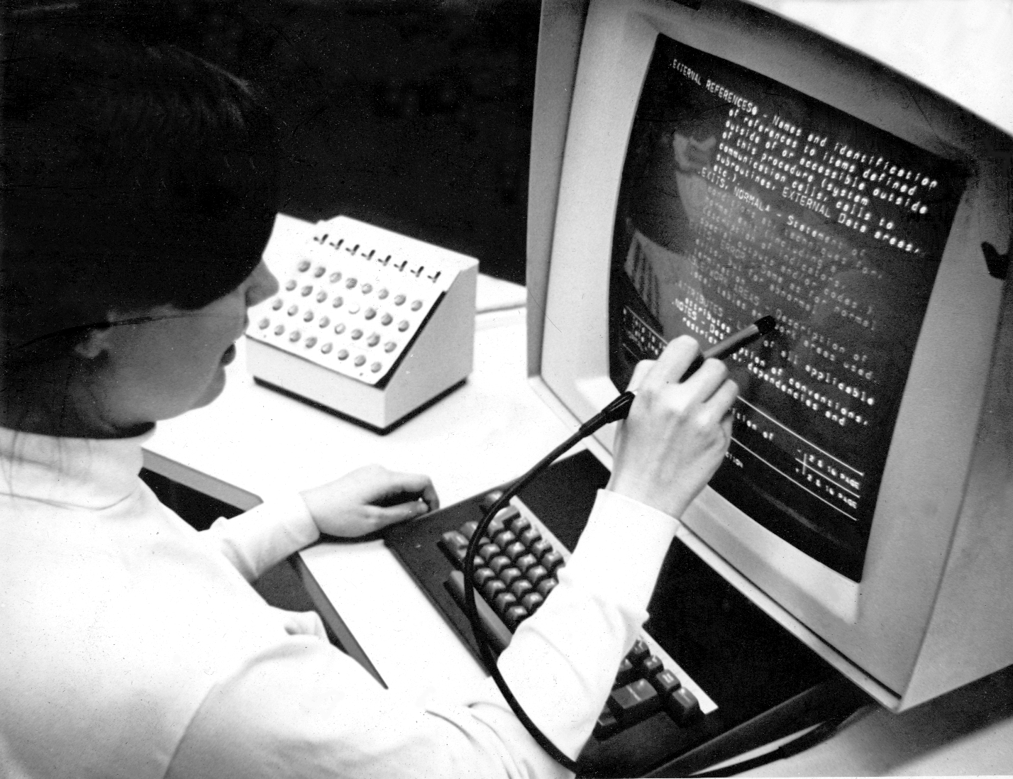 black and white photo: woman in 1969 using a stylus on a old-style monitor