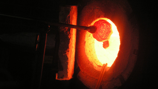A dark photo of rounded glass (bright orange) entering a kiln