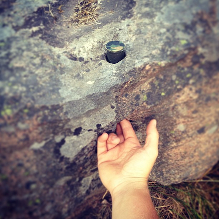 The photographer deomonstrates the mechanics of an ingenious hide: the container is recessed in a hole of a large boulder; it can only be accessed by pushing one's fingers through another hole on the side of the boulder.