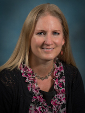 professional photo of Welhausen. She's looking at the camera and wearing a necklace, a black top, and a floral scarf.