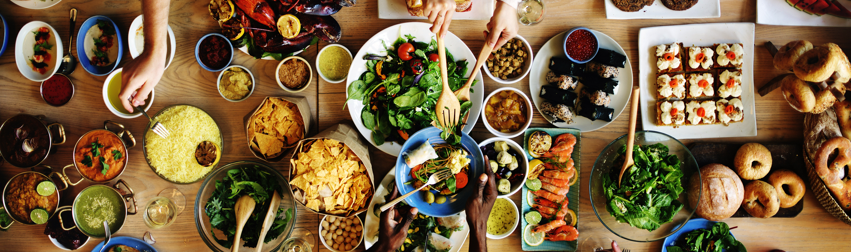 large table of food and hands are reaching out to taste each of the many dishes.