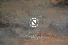 A rock painting with dancers, in white against a grey and orange rock