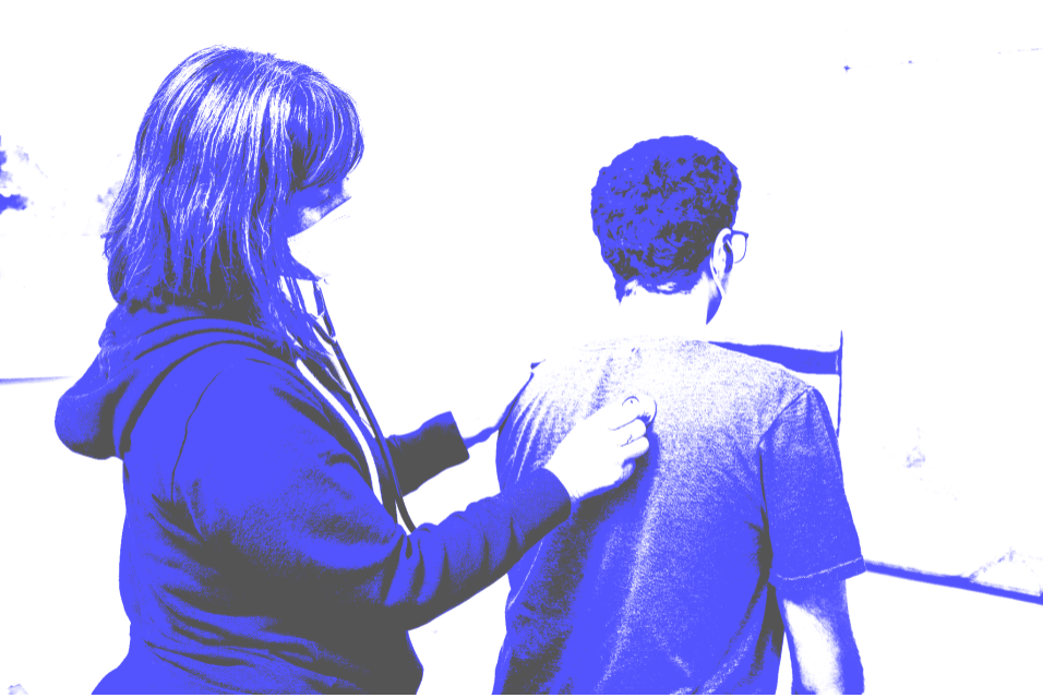 A blue and white image of a female doctor examining the back of a male patient with a stethoscope. The patient is sitting down and has his back to the viewer. He is wearing a tee shirt. The doctor is wearing a hoodie and a mask.