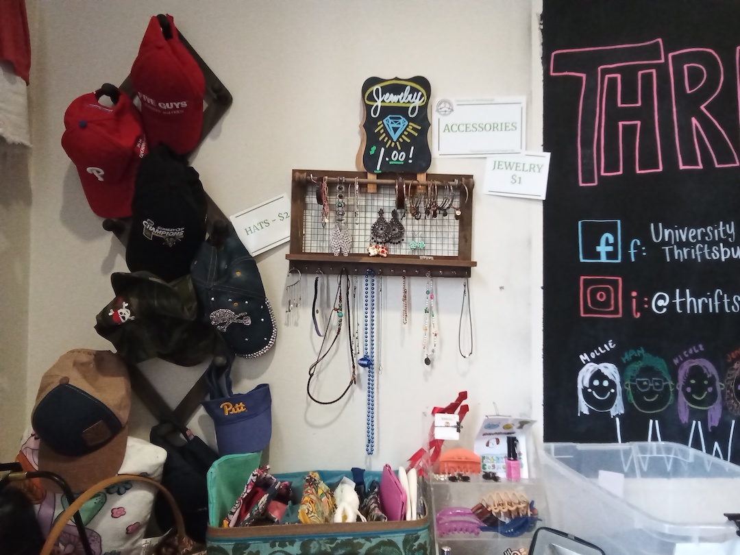 Various hats and jewelry hanging on white wall.