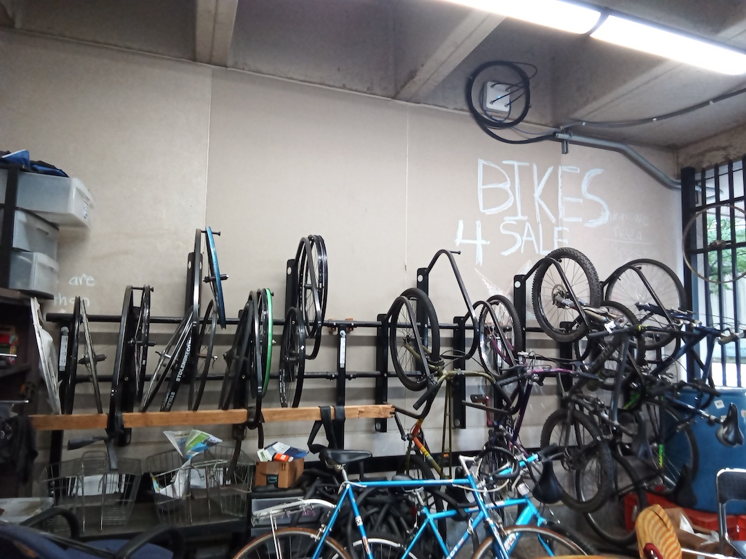 Many bikes and bike parts hanging on a wall, with Bikes 4 Sale written on the wall
