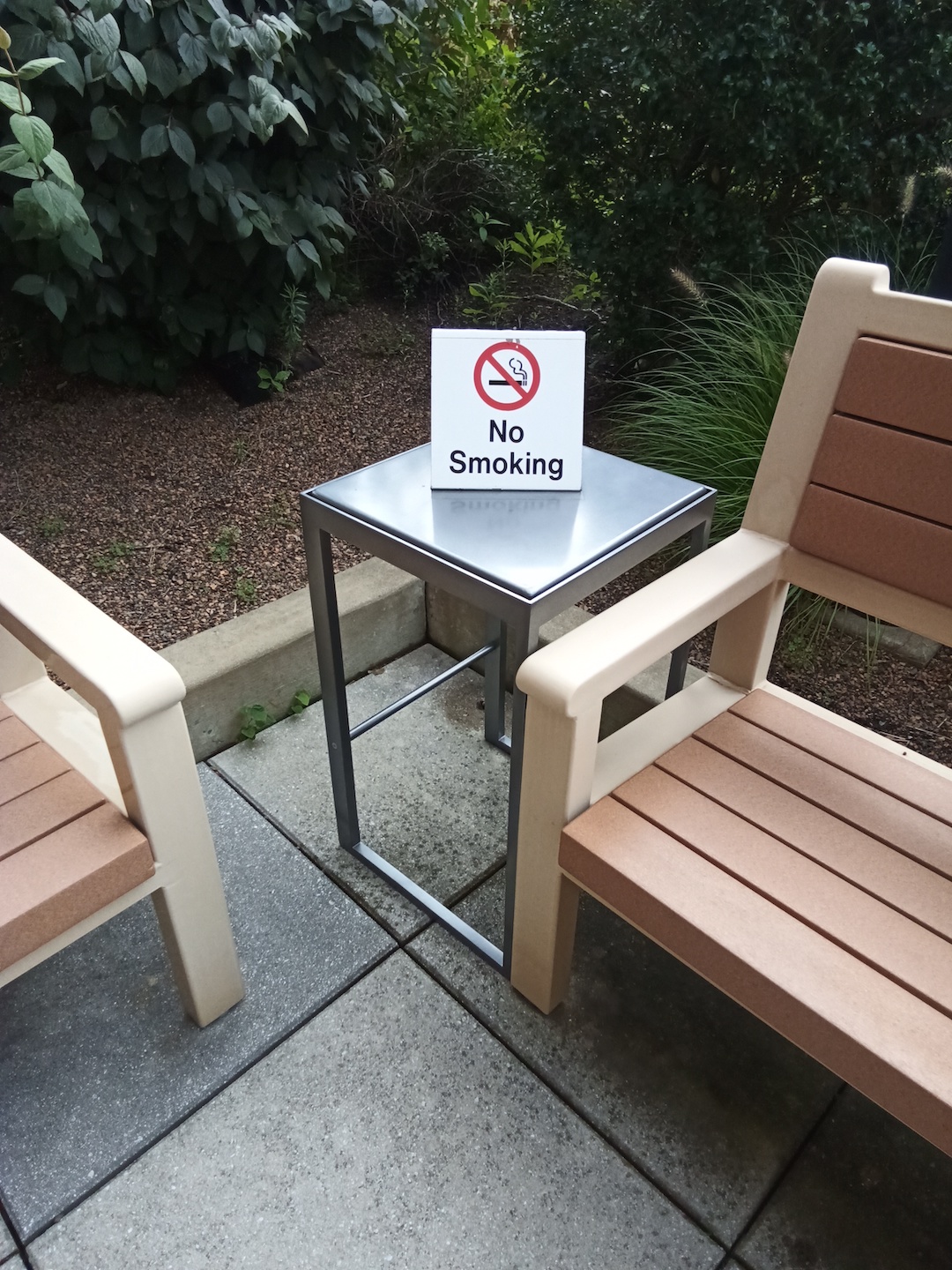 a no-smoking sign sitting on an outdoor table between benches