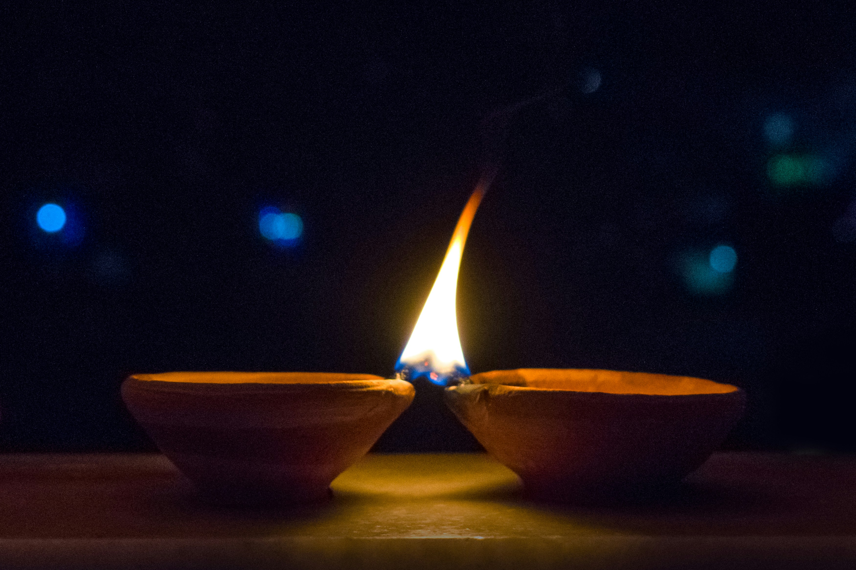 Two clay candle bowls with wicks touching share a single flame.