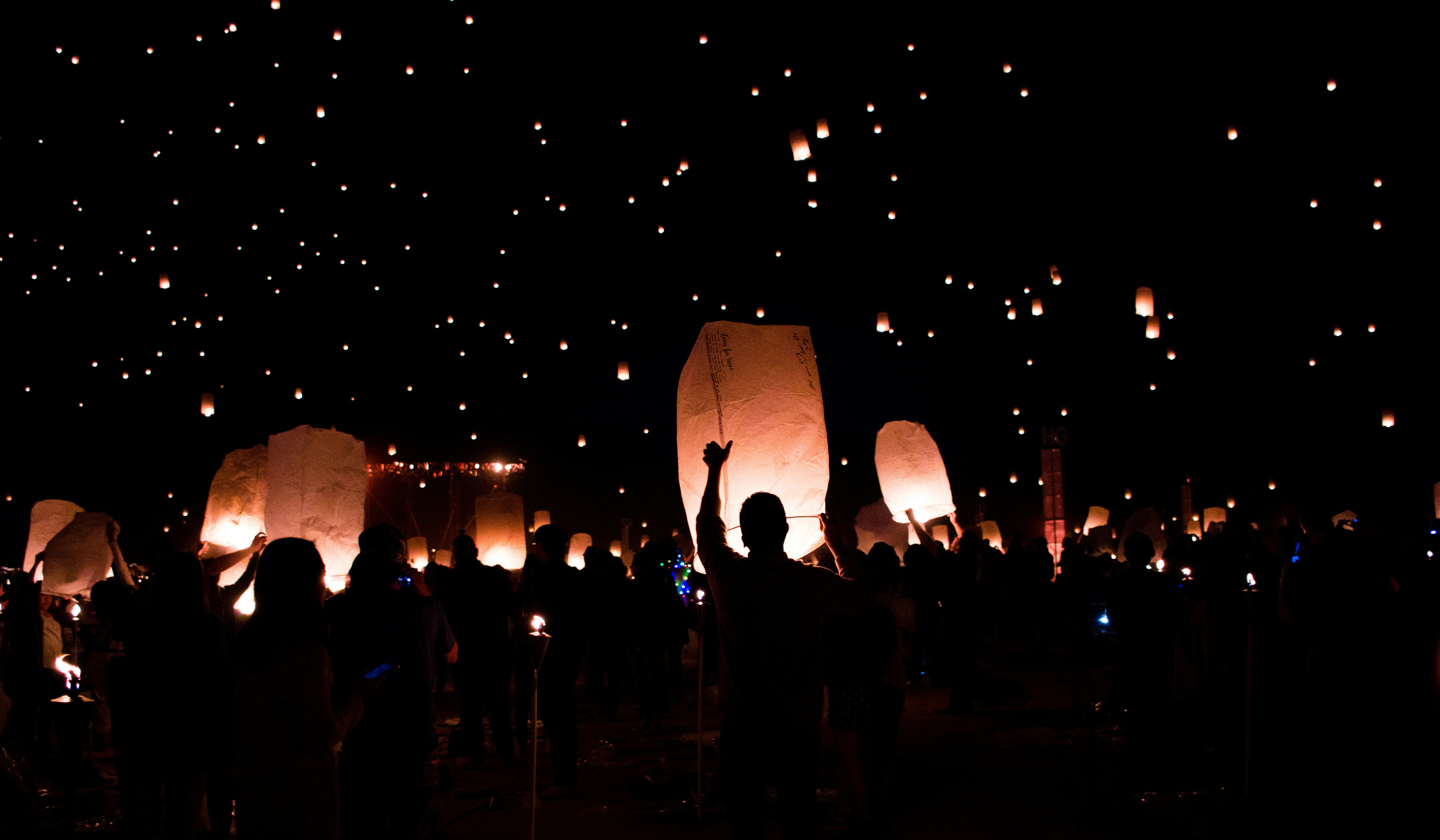 A crowd of people release paper lanterns into the night sky.